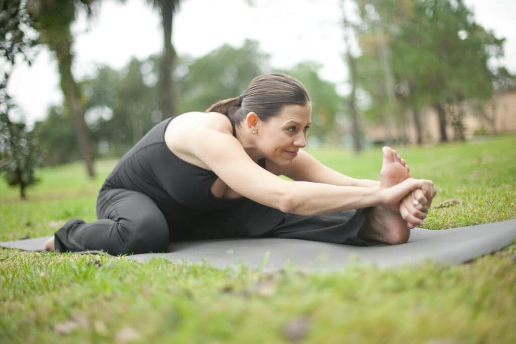 A pregnant yoga student practices a seated yoga pose from the Ashtanga Yoga primary series outdoors at The Yoga Shala in Maitland, Florida. She receives guidance from owner Krista Shirley, who specializes in supporting expectant mothers through modified yoga practices during pregnancy.