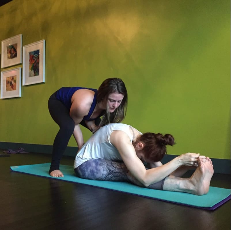 Yoga student receives an adjustment in Paschimottanasana posture, inside The Yoga Shala, 140 Circle Drive #4, Maitland, Florida, 32751. The studio provides personalized instruction and adjustments in small group classes.