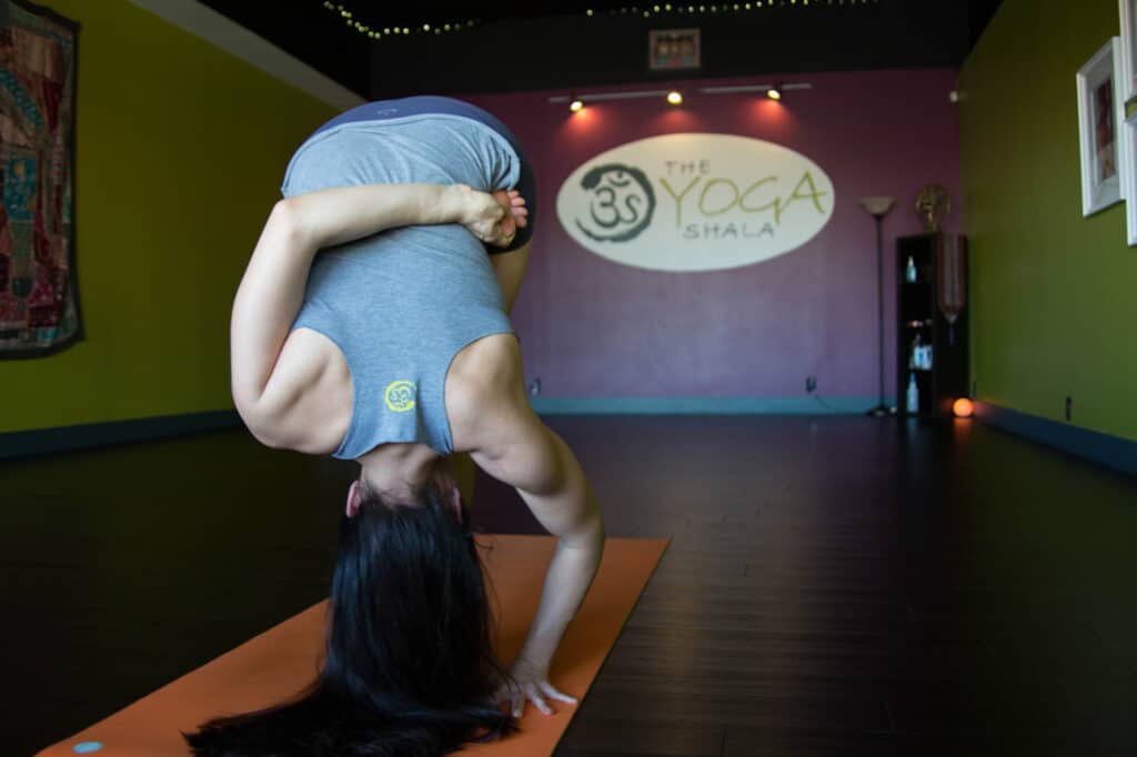 In her yoga studio, Krista Shirley, an authorized Level 2 Ashtanga Yoga teacher and owner of The Yoga Shala in Maitland, FL, gracefully embodies the full expression of Ardha Baddha Padma Padmottanasana, or Half Bound Lotus Forward Fold Pose. Krista specializes in traditional Ashtanga Yoga Mysore style teaching, offering students an authentic and transformative yoga experience. Additionally, she shares valuable insights and guidance on her YouTube channel (youtube.com/@yogawithkrista), supporting individuals in establishing and maintaining a safe and fulfilling at-home yoga practice.