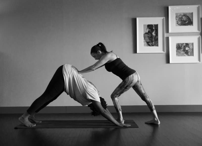 A yoga instructor from The Yoga Shala at 140 Circle Drive #4 in Maitland, FL, assisting a student in downward-facing dog pose during a yoga class.