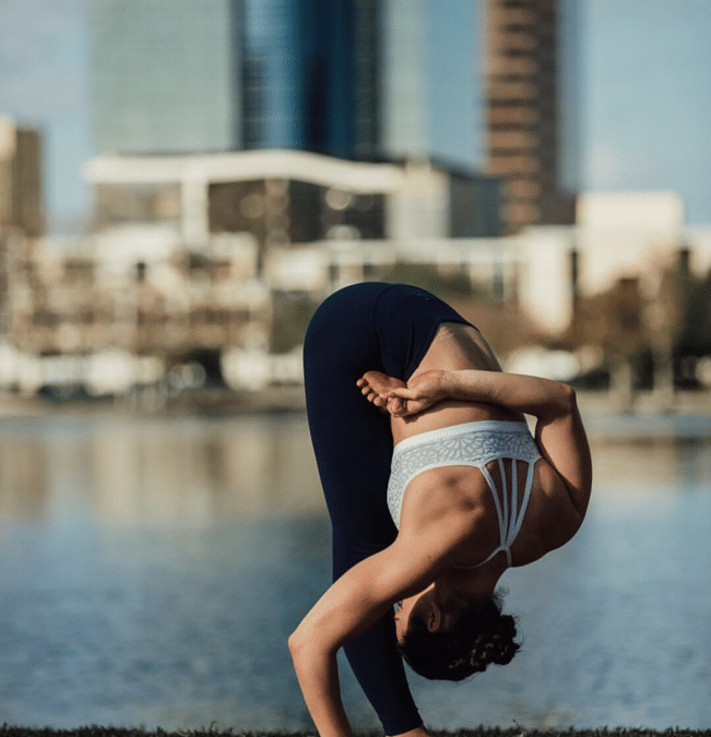 In the image, Krista Shirley, an authorized Level 2 Ashtanga Yoga instructor, is performing Ardha Baddha Padma Padmottanasana, or Half Bound Lotus Forward Fold Pose, against the serene backdrop of Lake Eola in downtown Orlando, Florida. Krista owns and operates the Yoga Shala, located at 140 Circle Drive #4, Maitland, FL, where she specializes in traditional Ashtanga Yoga Mysore style teaching, as well as rehabilitative body mechanics and mat pilates. Join Krista for classes in-person or virtually every weekday morning at The Yoga Shala. You can also find her sharing valuable insights and guidance on her YouTube channel (youtube.com/@yogawithkrista), helping individuals establish and maintain a safe and fulfilling at-home yoga practice.